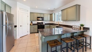 A kitchen with a central island, bar stools, a stainless steel refrigerator, and light green cabinets. - Newly Renovated Mountain Getaway Stocked for Fun! - (Flagstaff)
