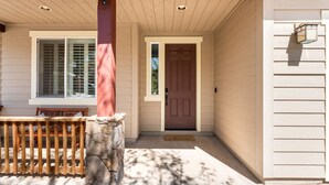 A house entrance with a wooden bench, a stone pillar, a brown door, and a window with blinds. - Newly Renovated Mountain Getaway Stocked for Fun! - (Flagstaff)