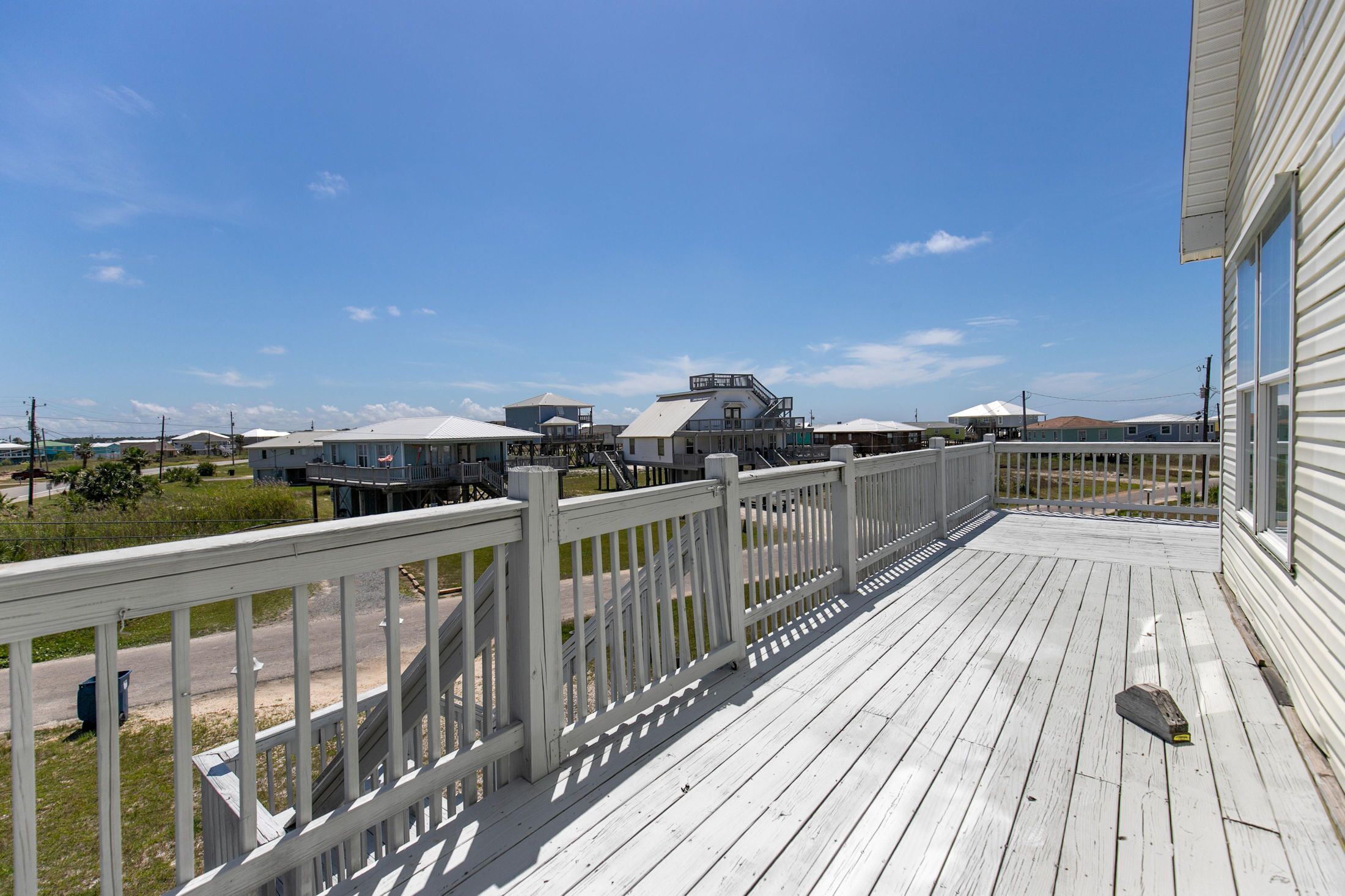 A wooden deck with a white railing, overlooking a row of houses and a clear blue sky.