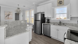 A modern kitchen with white cabinetry, granite countertops, stainless steel appliances, and a view of the outdoors through large windows.