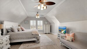 A bedroom with a bed, a sofa, a TV, and two ceiling fans.