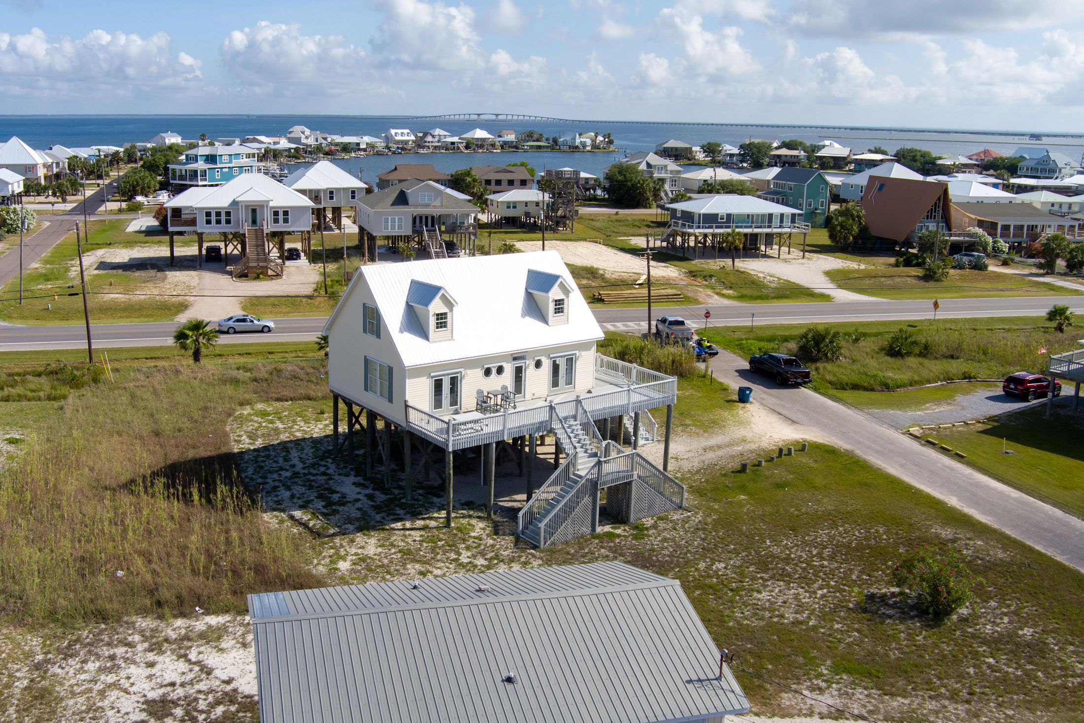 A coastal house with a balcony, a staircase, and a view of the ocean and a bridge in the background.