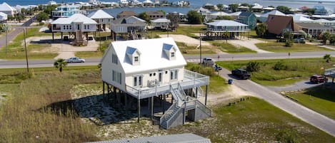 A coastal house with a balcony, a staircase, and a view of the ocean and a bridge in the background.