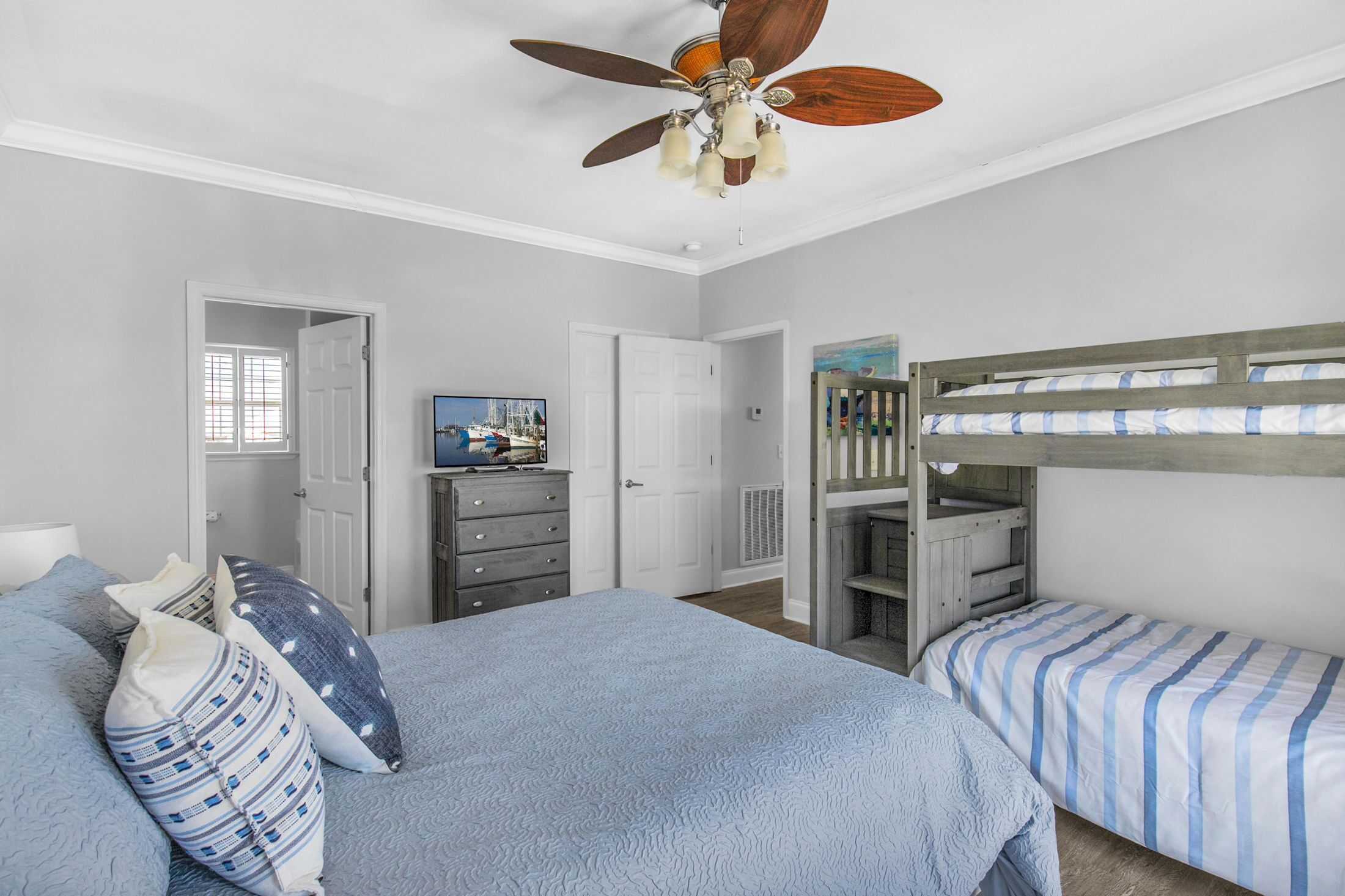 A bedroom with a bunk bed, a single bed, a ceiling fan, a dresser, and a television.