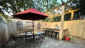 An outdoor patio with a round table, chairs, a red umbrella, and string lights. - Historic Annapolis Union House with Private Patio & Free Off-Site Parking (Annapolis)