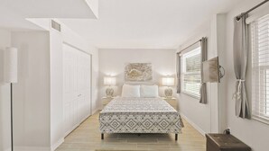 A bedroom with a bed, bedside lamps, a rug, a bench, and a painting on the wall.