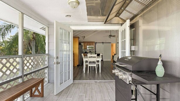 A balcony with a grill, a dining area, and a kitchen visible through an open door.