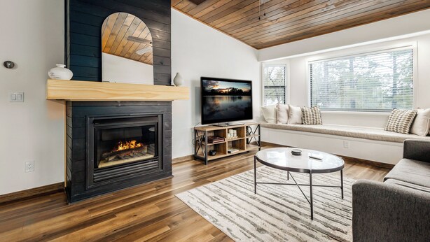 A living room with a fireplace, a television, a sofa, and a window with blinds.