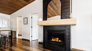 A modern living room with a fireplace, wooden flooring, and a dining area with stools.