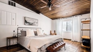 A bedroom with a bed, a bench, a nightstand, a ceiling fan, and a window with blinds.