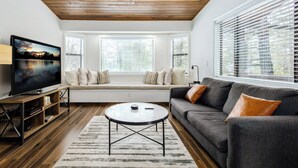 A modern living room with a wooden ceiling, a large flat-screen TV, a grey sofa, and a round coffee table.