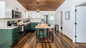 A modern kitchen with wooden flooring, green cabinets, and a central island with stools.