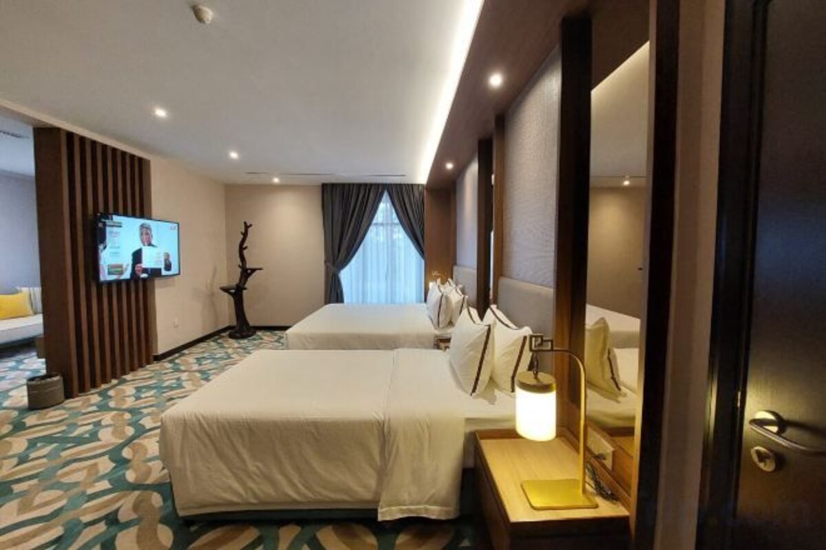 A hotel room with two beds, a TV, a desk with a lamp, and a window with curtains.