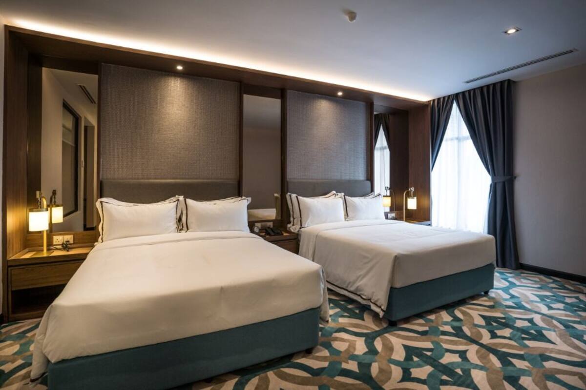 A hotel room with two beds, a large mirror, a nightstand with a lamp, and a patterned carpet.