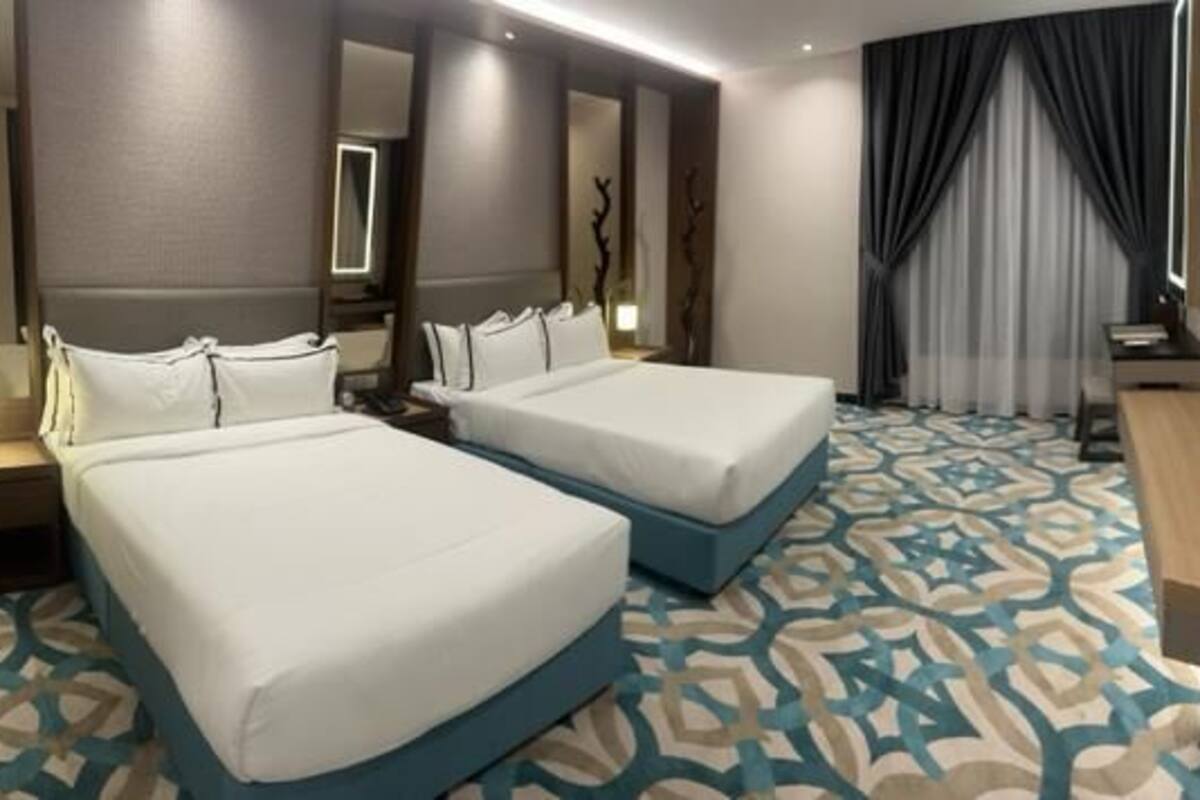 A hotel room with two beds, a desk, a chair, a TV, and a patterned carpet.