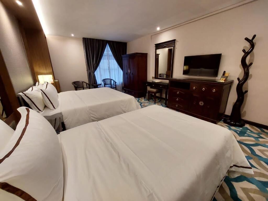 A hotel room with two beds, a desk, a chair, a television, and a mirror.