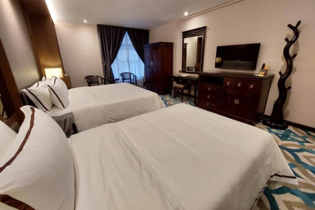 A hotel room with two beds, a desk, a chair, a television, and a mirror.