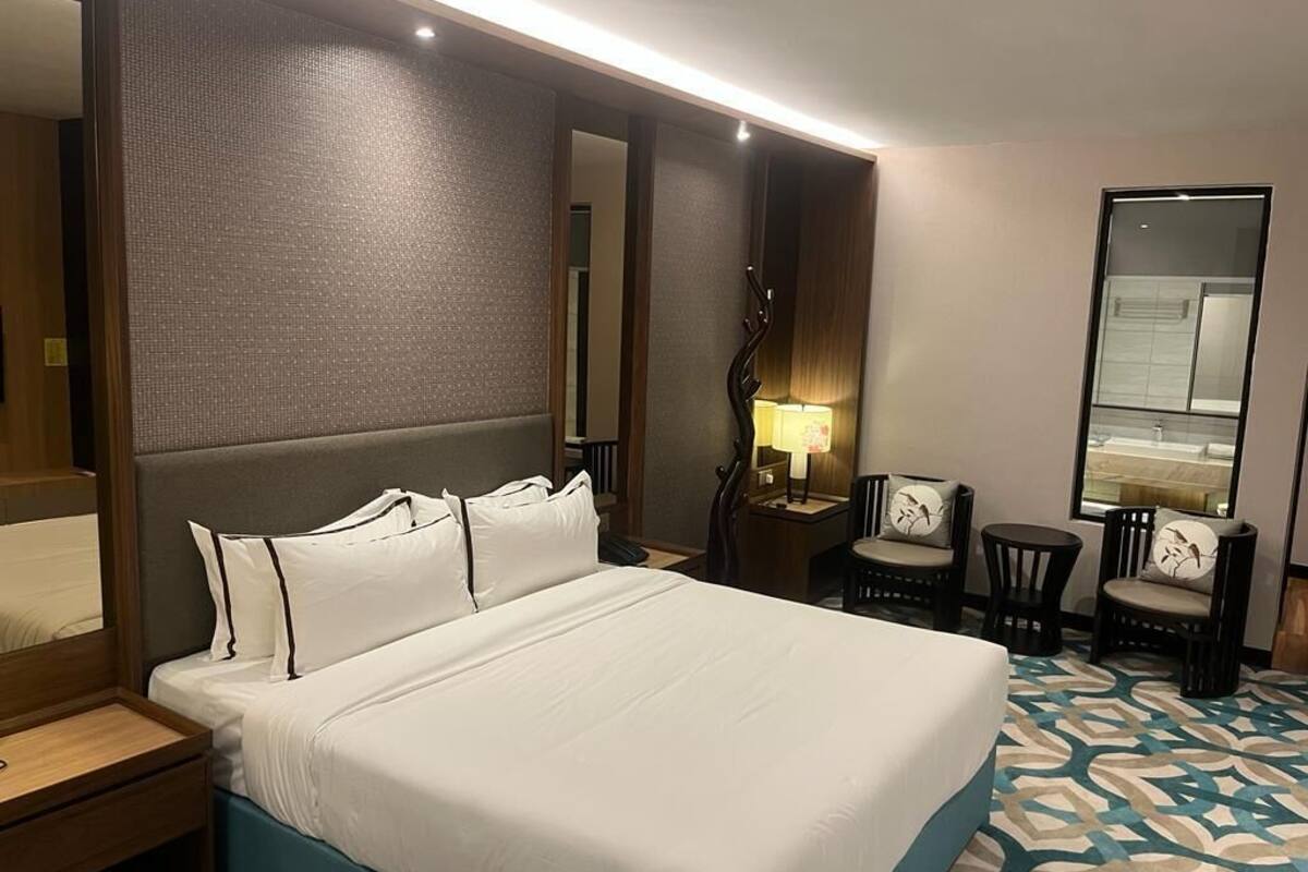 A hotel room with a large bed, a bedside table, a lamp, two chairs, and a mirror.