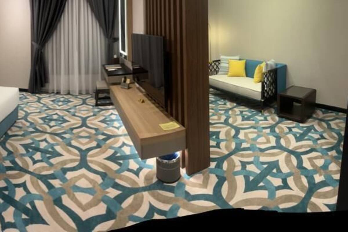 A hotel room with two beds, a desk, a TV, and a patterned carpet.