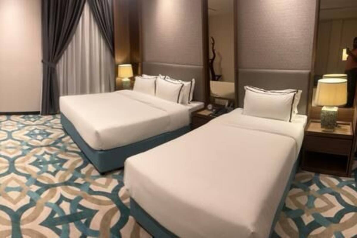 A hotel room with two beds, a sofa, and a patterned floor.