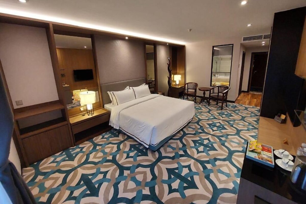 Habitación de hotel con cama, mesitas de noche, un escritorio con silla, televisor y una alfombra estampada.