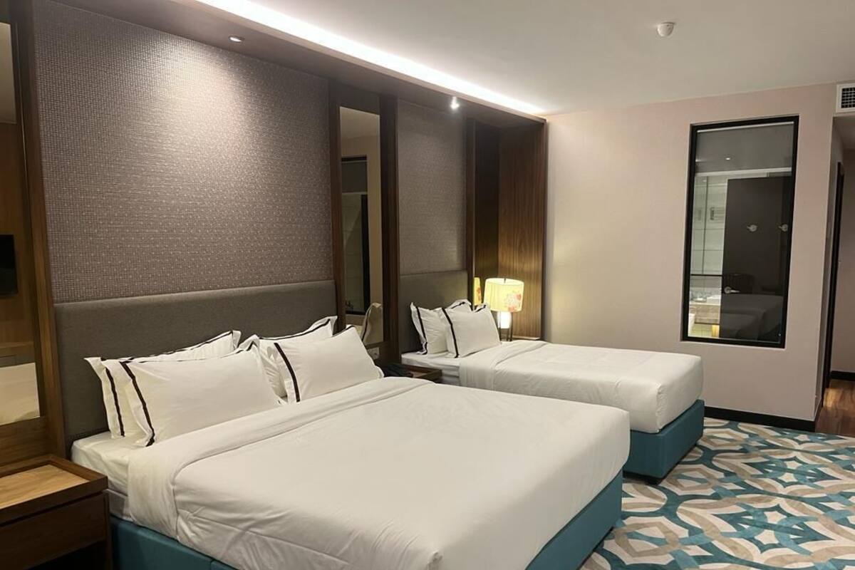 A hotel room with two beds, a large mirror, a nightstand, and a patterned carpet.