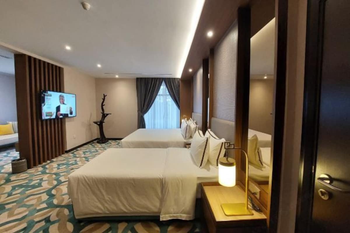 A hotel room with two beds, a television, a desk with a lamp, and a patterned carpet.