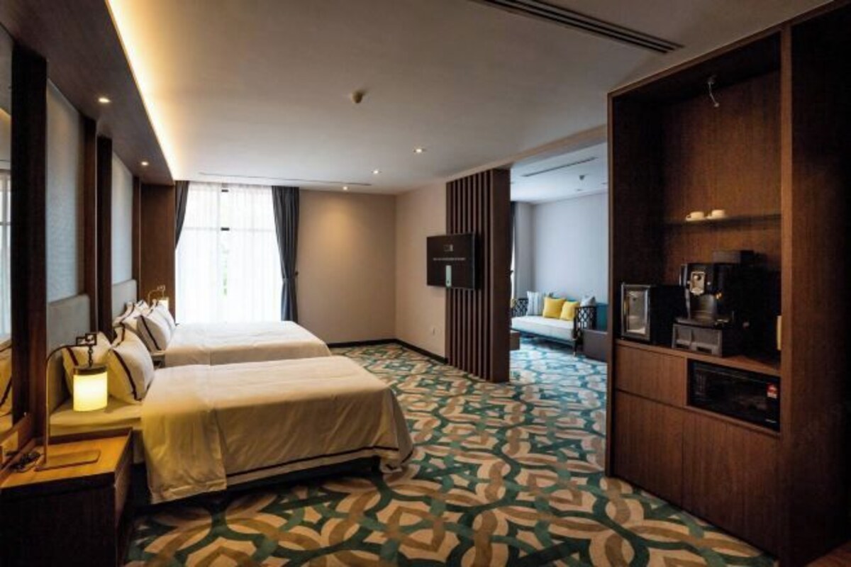 A hotel room with two beds, a TV, a coffee machine, and a patterned carpet.
