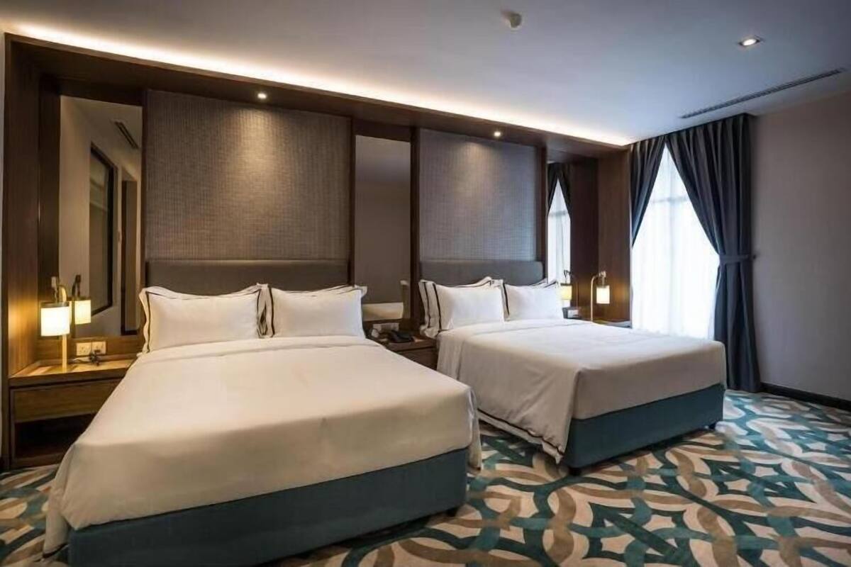 A hotel room with two beds, a large mirror, and a patterned carpet.