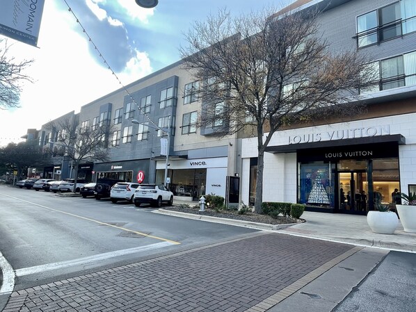 A street view with a Louis Vuitton store, parked cars, and a VINCÉ store.