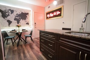 Une cuisine moderne avec des meubles en bois foncé, un comptoir en granit et un évier en acier inoxydable. On y trouve une table à manger avec des chaises et une carte du monde accrochée au mur.