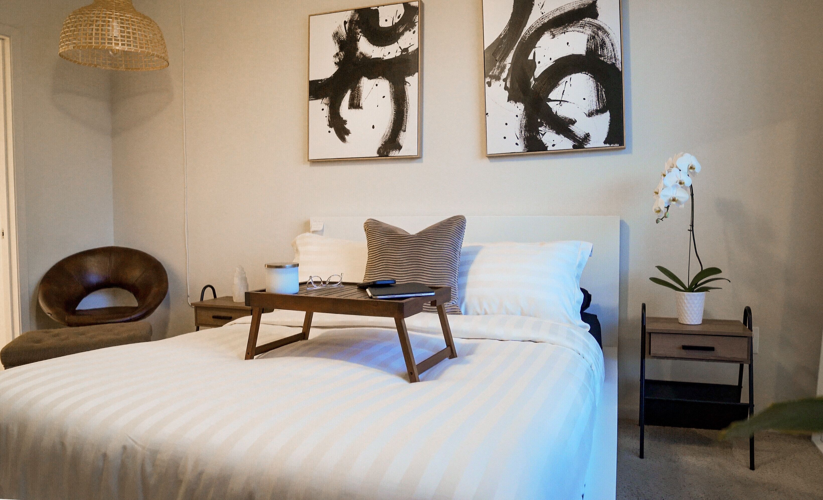 Un dormitorio con una cama, mesitas de noche, una lámpara y una obra de arte en la pared.