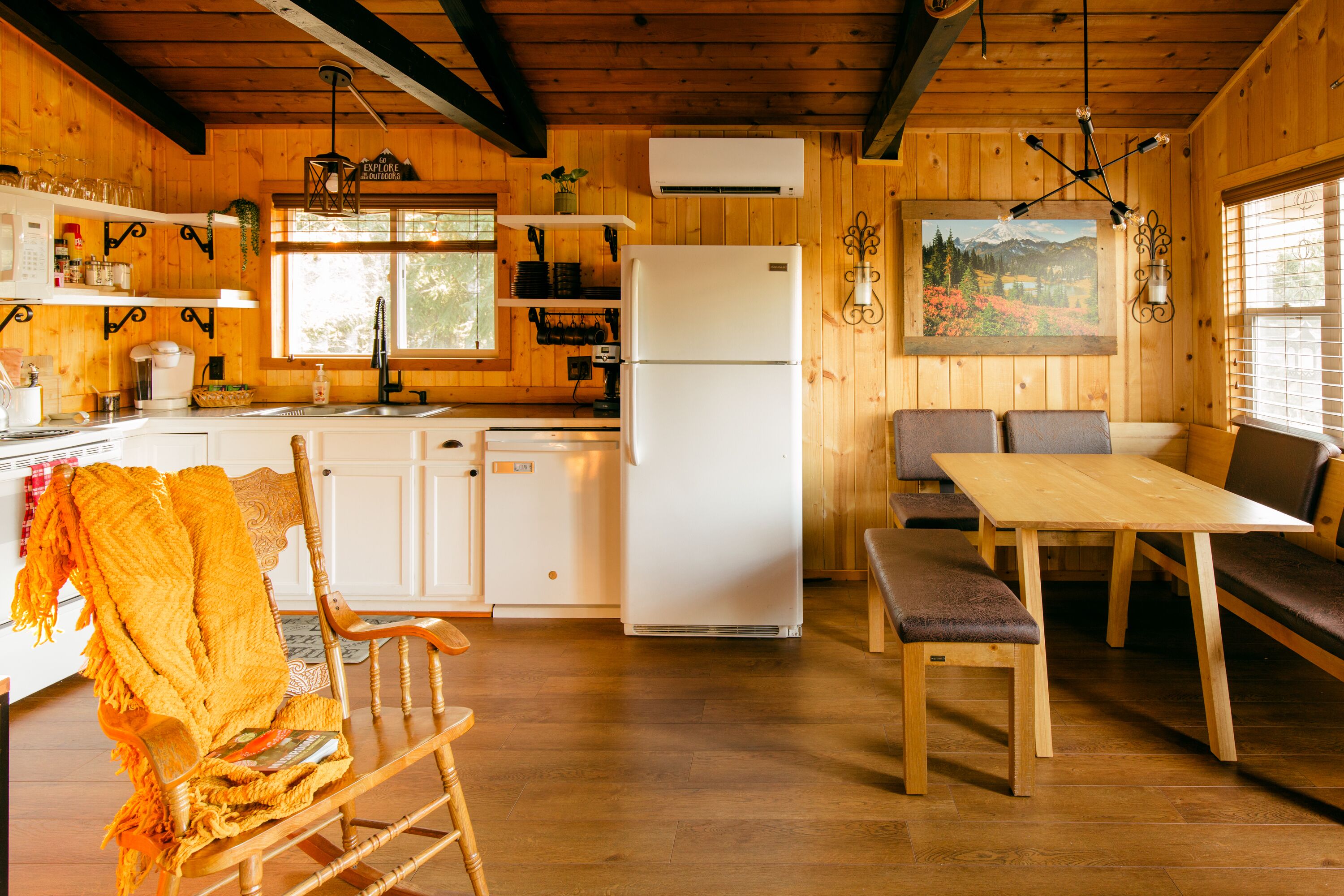 A cozy cabin-style kitchen with wooden walls, a white refrigerator, and a dining area with a bench and table.