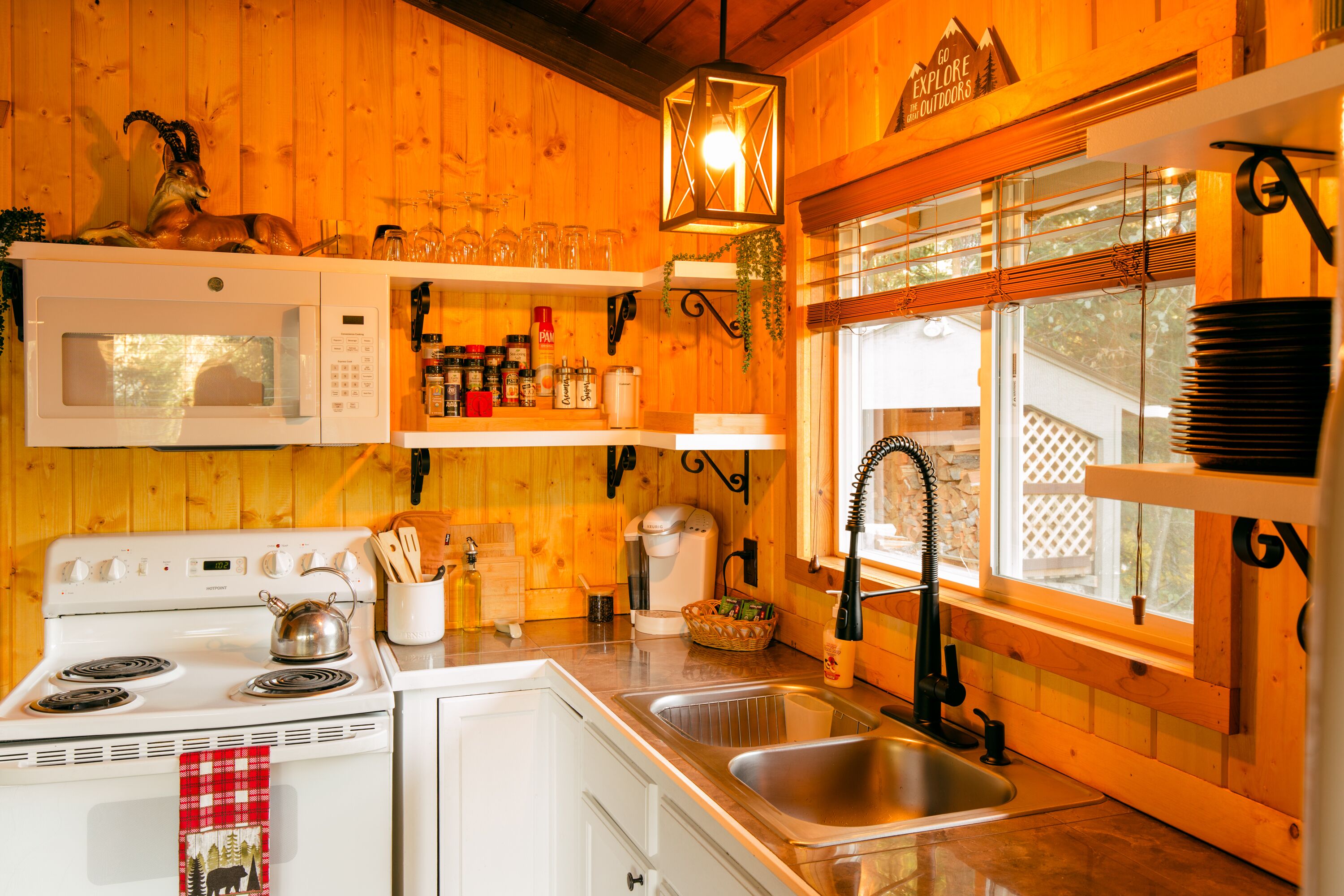 A kitchen with wooden walls, a stove, a microwave, a sink, and various kitchen items.