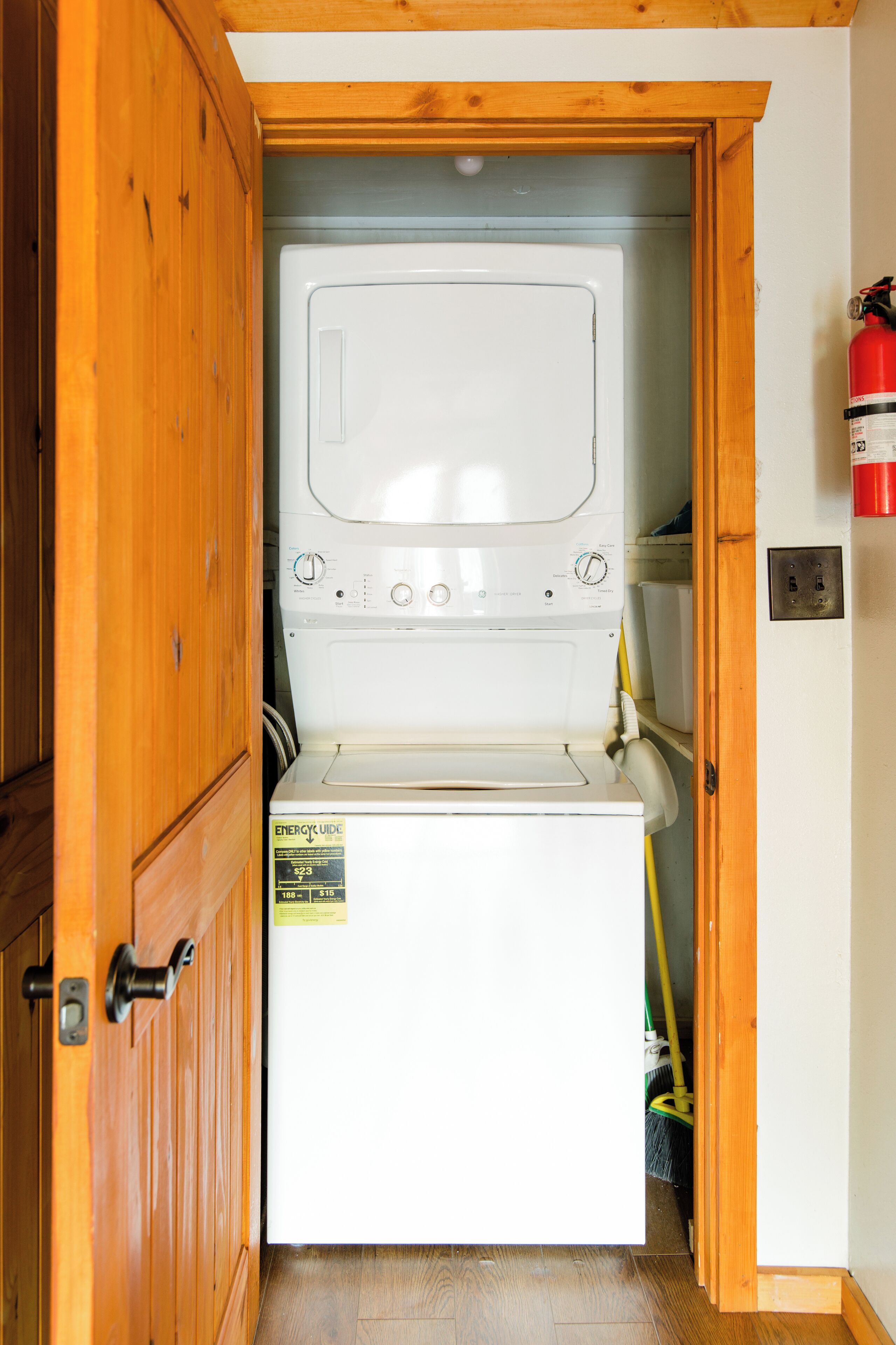 Une petite buanderie avec un lave-linge blanc, des armoires en bois et un extincteur fixé au mur.