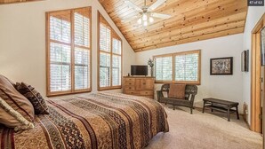 A bedroom with a large bed, wooden ceiling, and large windows. - Deer Meadow Cabin @ Shaver Lake (Shaver Lake)