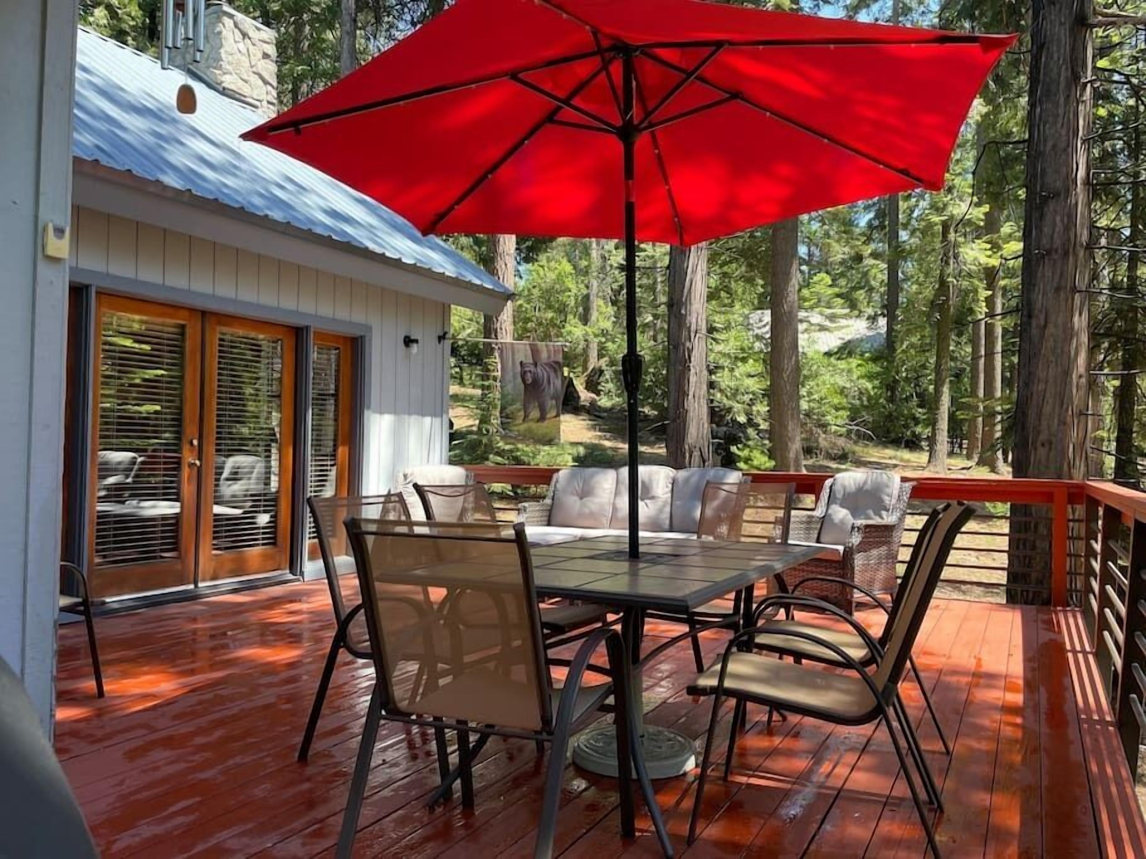 Una terraza al aire libre con un paraguas rojo, una mesa y sillas.