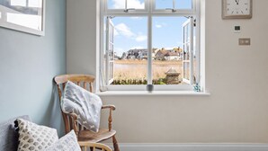 A room with a large window, a wooden chair, and a clock on the wall.