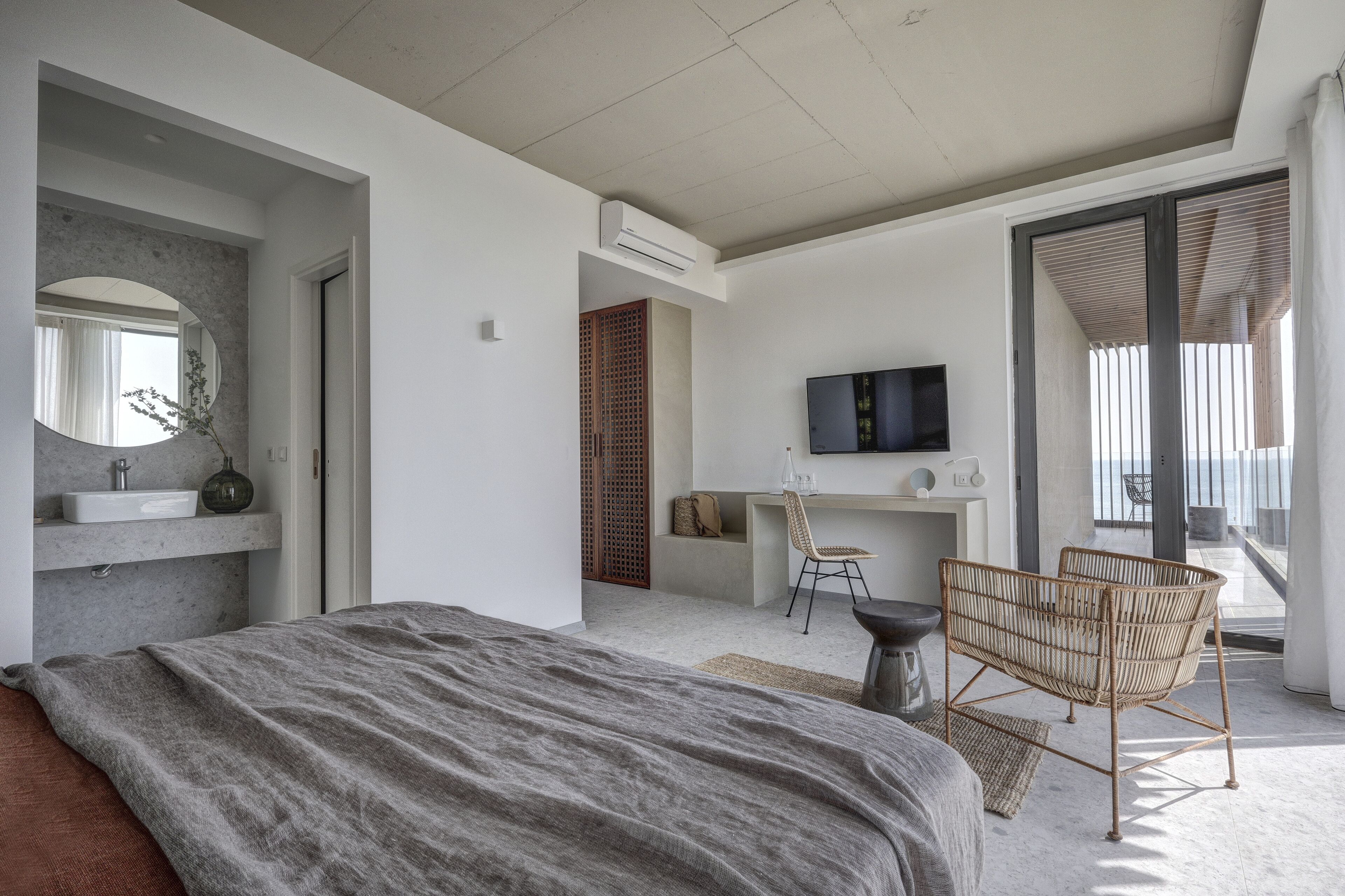 A modern bedroom with a large bed, a desk, a chair, and a TV.