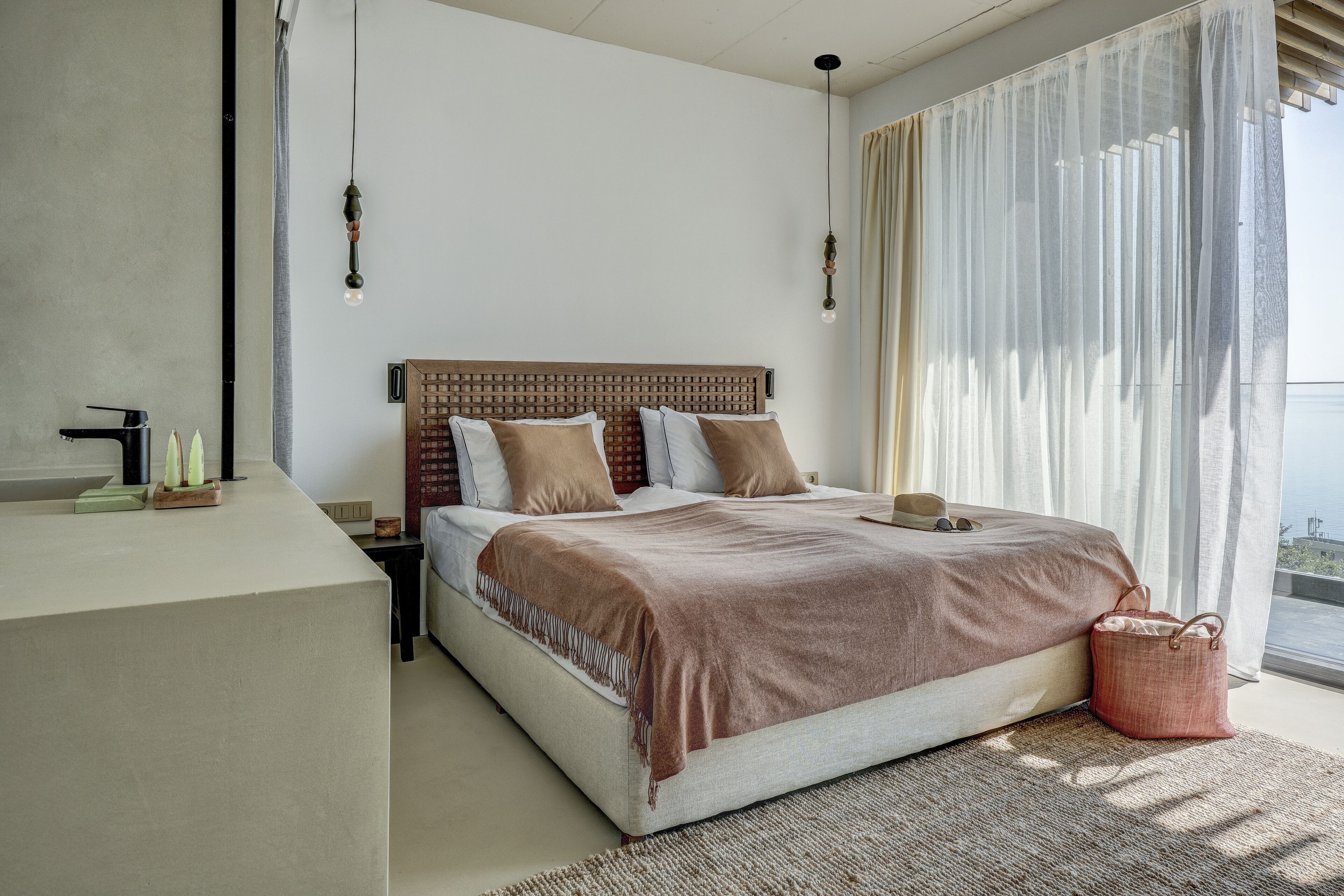 Un dormitorio moderno con una cama grande, una mesita de noche y cortinas traslúcidas que ofrecen vistas al exterior.