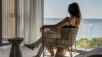 A person sitting in a wicker chair by a window overlooking a body of water.