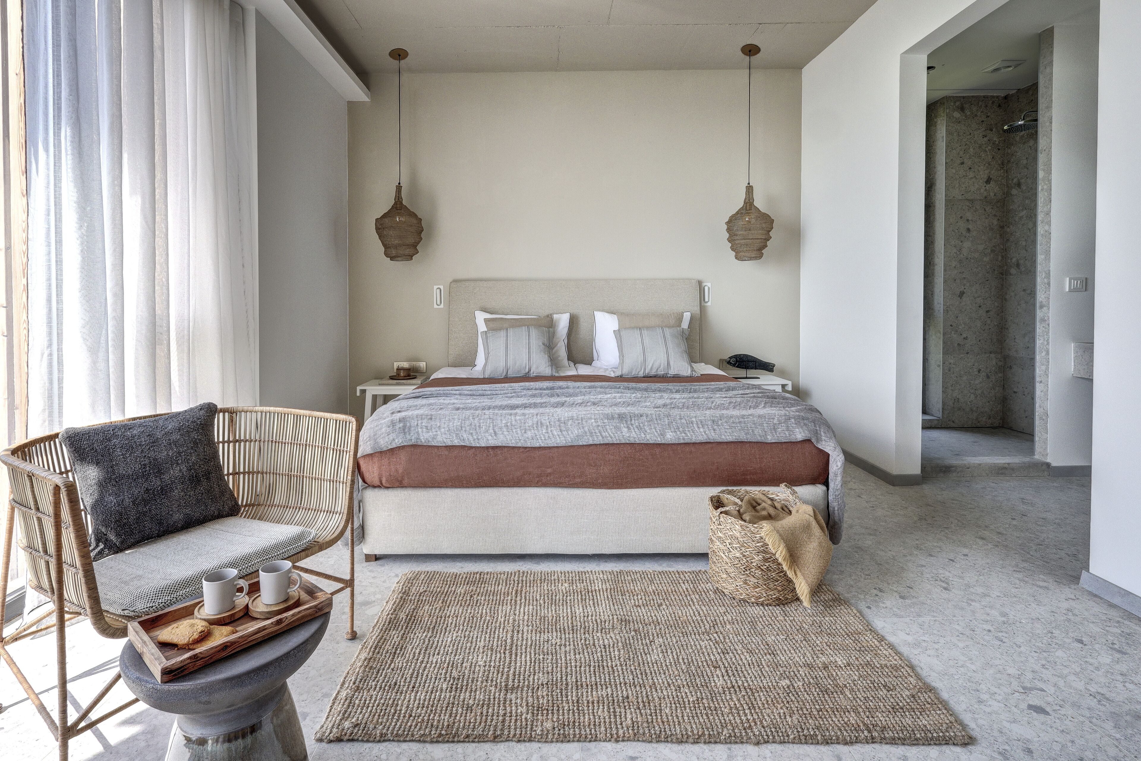 Un dormitorio con cama, mesitas de noche, una silla de mimbre y un tapete tejido.