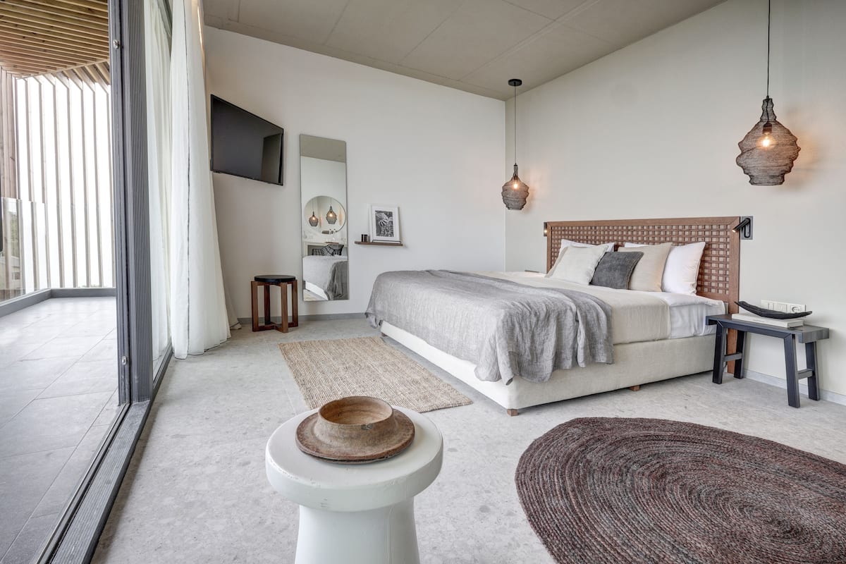 Ein modernes Schlafzimmer mit einem großen Bett, Nachttischen, einem Spiegel und Blick durch eine Glastür.