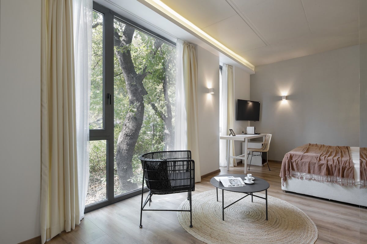 Ein modernes Zimmer mit großem Fenster, einem schwarzen Sessel, einem kleinen Tisch, einer Couch und einem Fernseher.