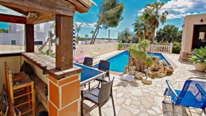 An outdoor pool area with a table and chairs, surrounded by stone tiles and palm trees.