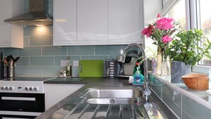 Une cuisine moderne dotée d’un évier en acier inoxydable, d’une cuisinière et d’une planche à découper verte.