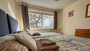 Une chambre avec deux lits, une fenêtre avec des rideaux, un radiateur et une commode en bois.