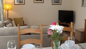 Un coin repas avec une table dressée pour deux personnes, un téléviseur en arrière-plan et un canapé dans le salon.