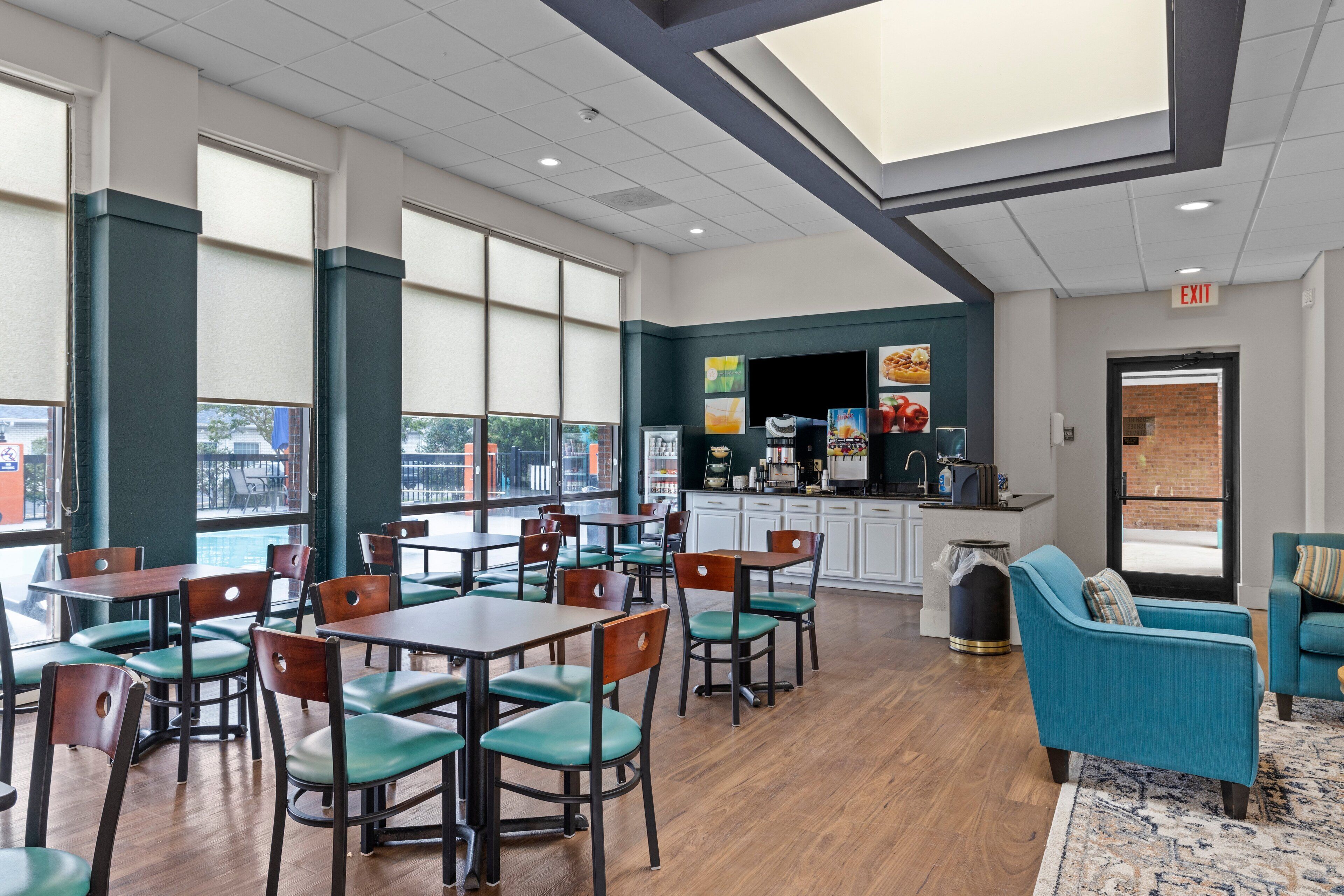 A restaurant with wooden tables and green chairs, a kitchen area, and a seating area with teal sofas.