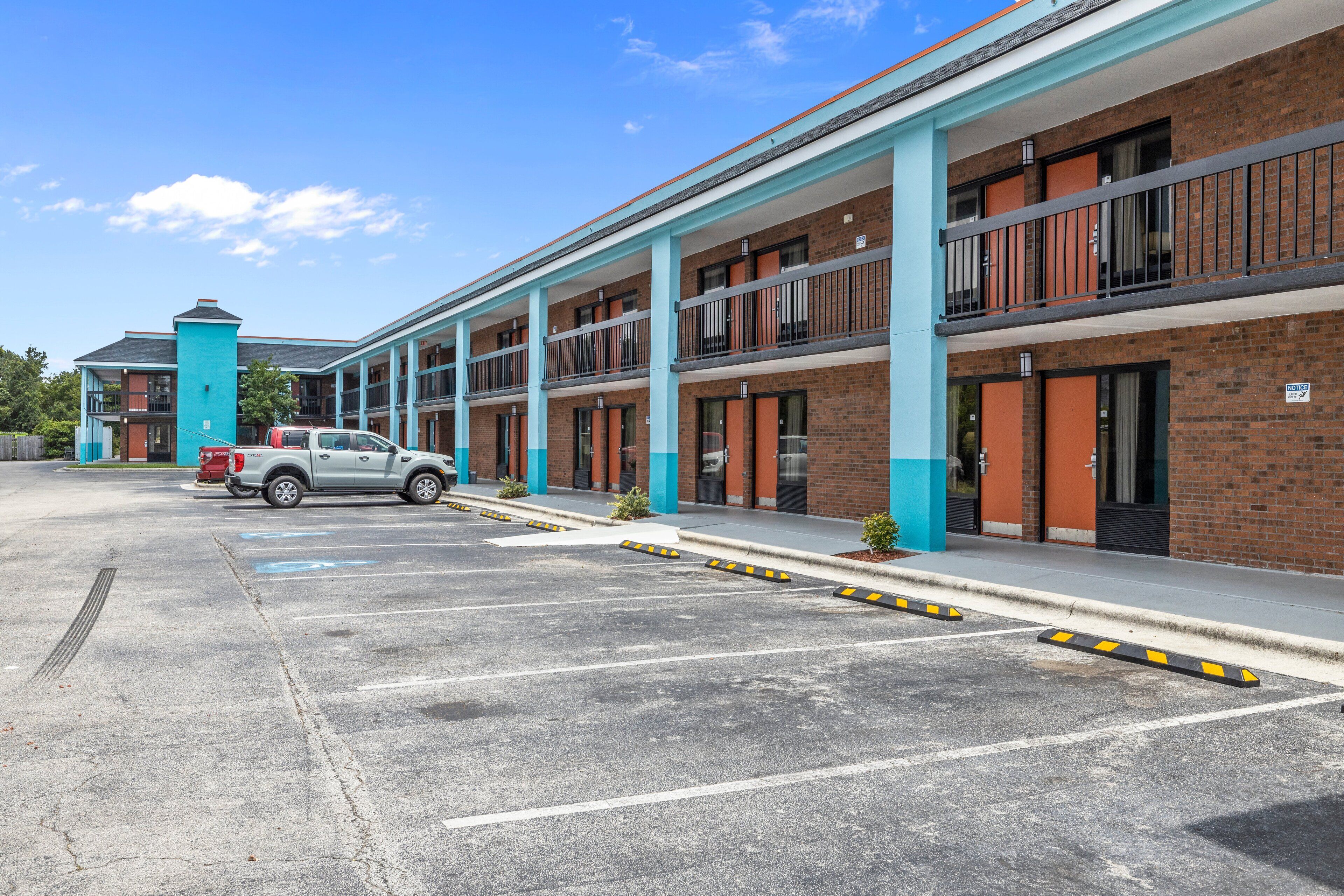 A multi-story motel with a brick facade, blue accents, and a parking lot with a white truck.